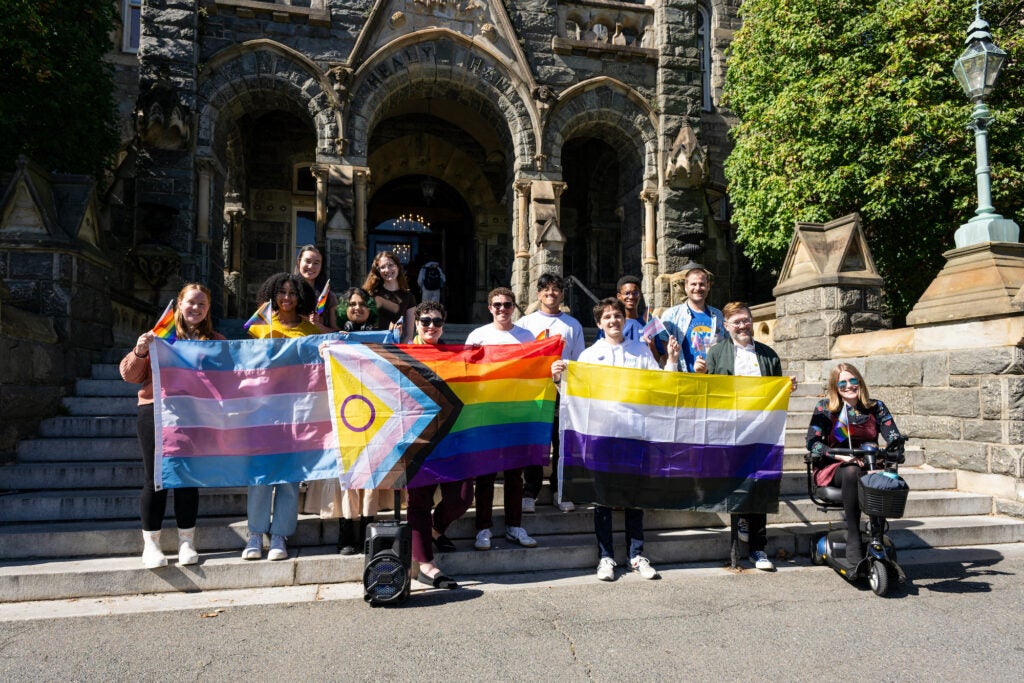 Students and staff gather for a group photo in front of Healy Hall, holding pride flags.